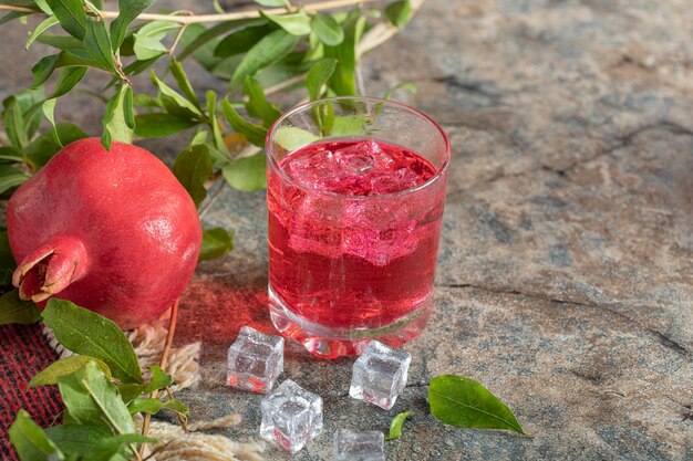 Succo ghiacciato e melograno con foglie su sfondo di pietra