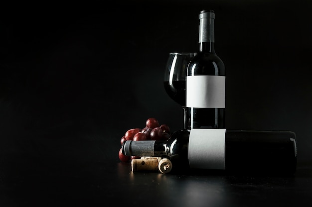 Sugheri e uva vicino bottiglie e bicchiere di vino