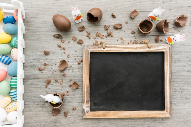 Superficie di legno con ardesia, conigli e uova di cioccolato per il giorno di Pasqua