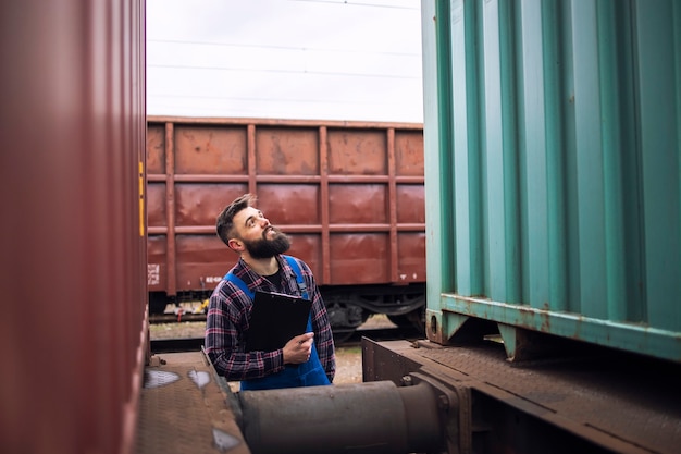 Supervisore del lavoratore ferroviario che ispeziona il container del carico di spedizione alla stazione dei treni merci