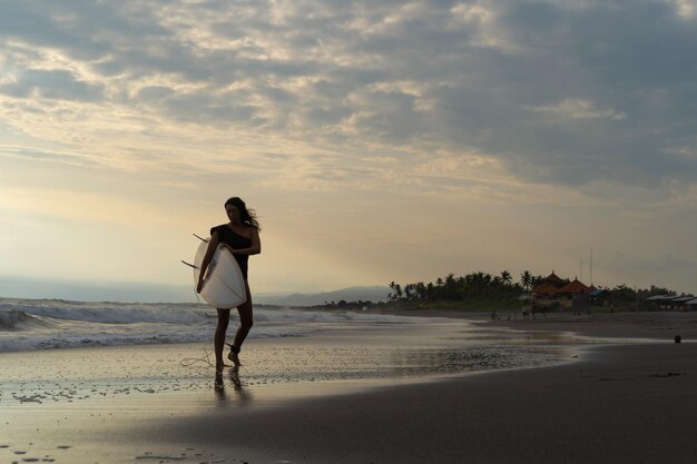 Surfista della donna con la tavola da surf sull'oceano al tramonto