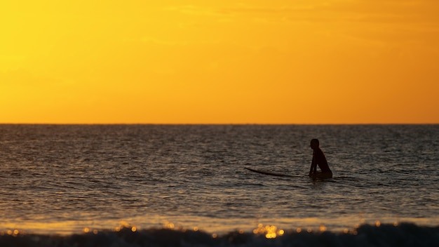 Surfista seduto nell'oceano al tramonto