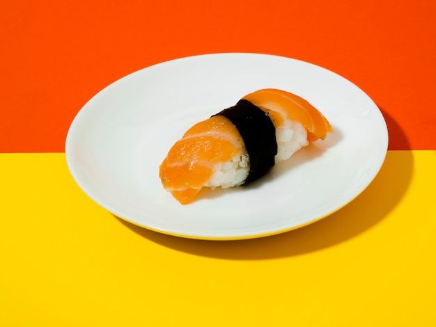 Sushi di color salmone su un piatto bianco su uno sfondo giallo e arancio