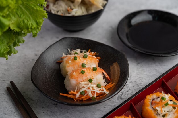 Sushi è in un piatto con le bacchette e salsa di immersione su un pavimento di cemento bianco.