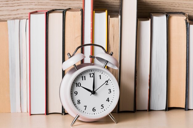 Sveglia bianca che mostra 10&#39;o orologio davanti allo scaffale per libri sullo scrittorio di legno