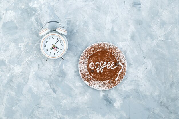 Sveglia e piastra con la parola caffè su uno sfondo grigio sgangherato