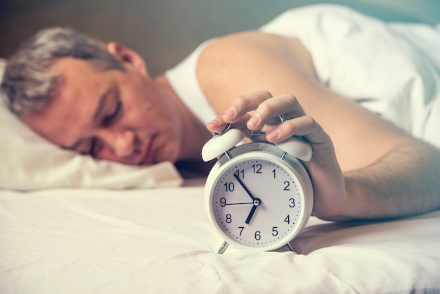 Svegliato. La mano spegne la sveglia che si sveglia alla mattina. Tono morbido della pelle. L&#39;uomo esausto è svegliato da una sveglia nella sua camera da letto