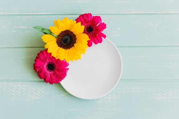 Svuoti il ​​piatto bianco decorato con il fiore della gerbera e del girasole sulla tavola