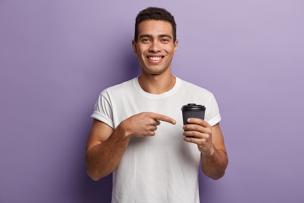 T-shirt bianca da portare del giovane uomo del brunet che indica alla tazza di caffè