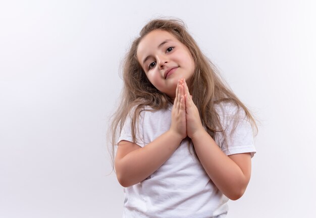T-shirt bianca da portare sorridente della bambina della scuola che mostra pregare il gesto su fondo bianco isolato