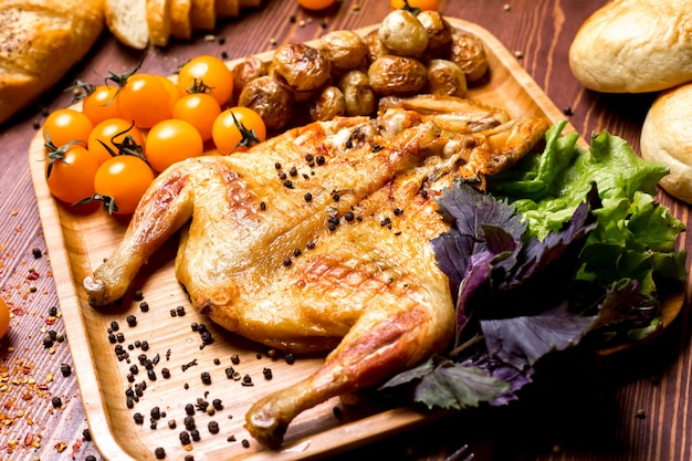 Tabacco di pollo di vista laterale con patate e pomodorini gialli con basilico su un vassoio