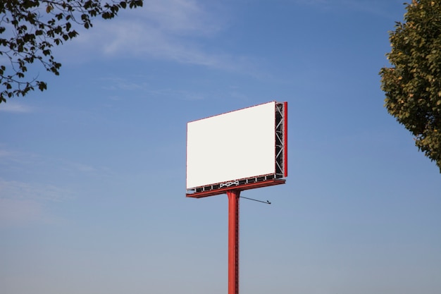 Tabellone per le affissioni in bianco bianco per la pubblicità contro cielo blu con gli alberi
