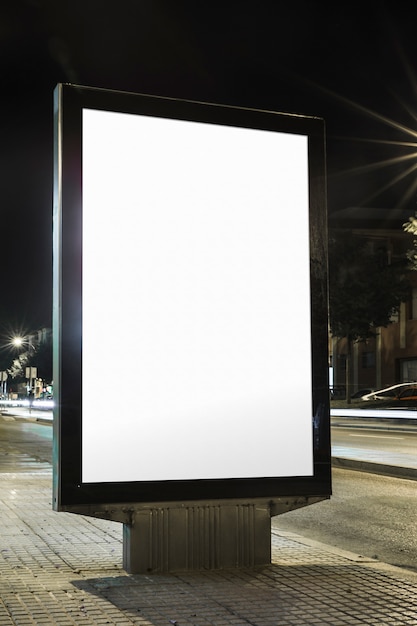 Tabellone per le affissioni in bianco con lo schermo bianco sul marciapiede alla notte