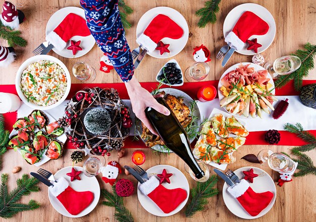 Tacchino al forno. Cena di Natale. La tavola di Natale è servita con un tacchino, decorato con orpelli luminosi e candele. Pollo fritto, tavola. Cena di famiglia. Vista dall'alto, mani nel telaio