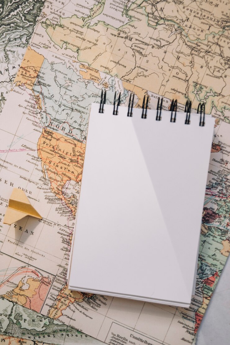 Foto gratuito taccuino del primo piano e aereo di carta sulla mappa