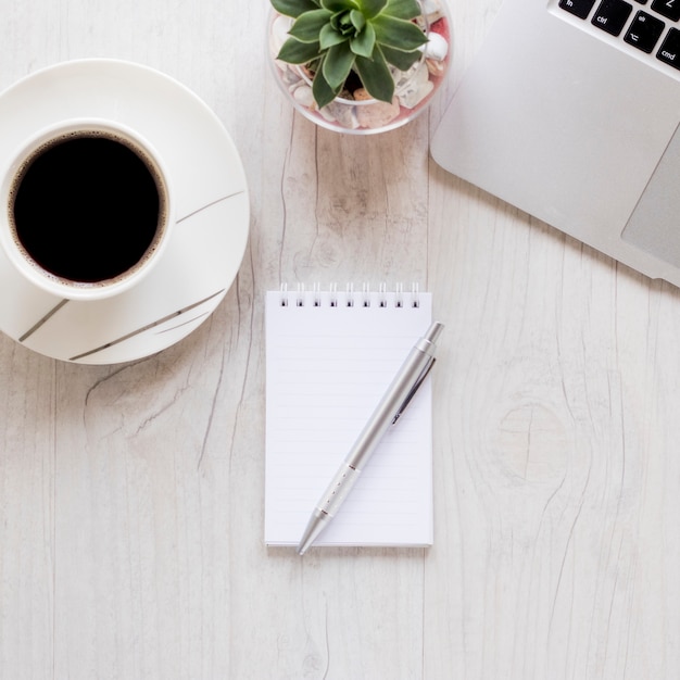 Taccuino del primo piano vicino a caffè e computer portatile