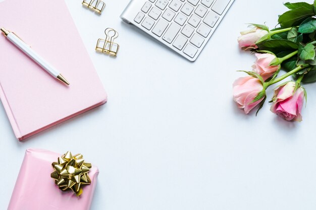 Taccuino rosa, una penna, una confezione regalo, una tastiera e rose rosa su sfondo bianco