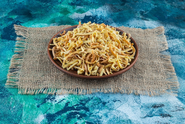 Tagliatella in una ciotola su una trama, sul tavolo blu.