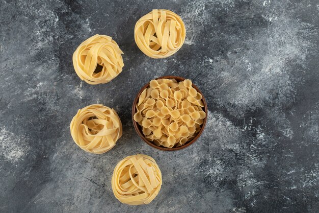 Tagliatelle a nido d'ape crudo con pasta di farfalle tonde su un tavolo di marmo.