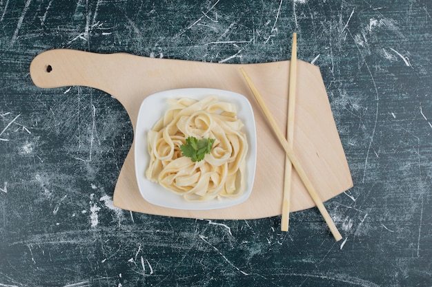 Tagliatelle bollite sul piatto bianco con le bacchette.