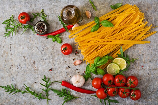 Tagliatelle di pasta e ingredienti per cucinare (pomodori, aglio, basilico, peperoncino). Vista dall'alto