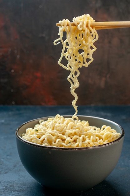 Tagliatelle di ramen asiatico vista frontale sollevate con le bacchette sul tavolo scuro