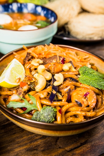 Tagliatelle di udon tailandesi saporite con manzo; broccoli; menta; noci e limone in una ciotola sul tavolo di legno