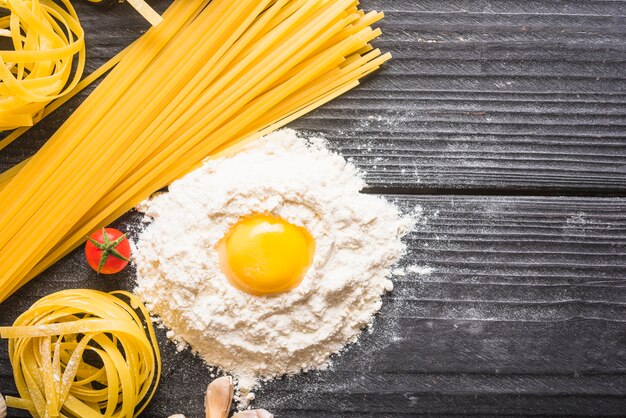 Tagliatelle e pasta cruda con ingredienti sul contesto in legno