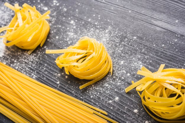 Tagliatelle e spaghetti crudi sul fondale in legno nero