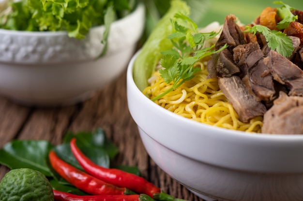 Tagliatelle gialle in una tazza con maiale croccante, fette di maiale e polpette insieme a tagliatelle tailandesi