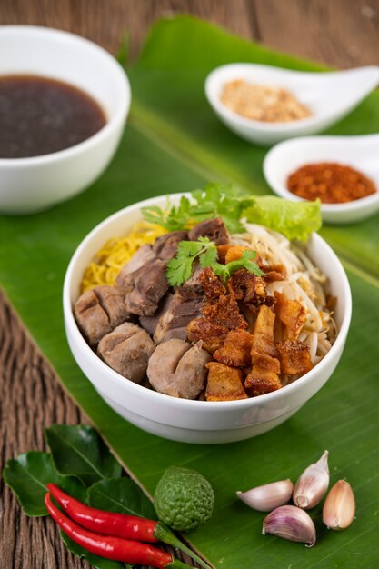 Tagliatelle gialle in una tazza con maiale croccante, fette di maiale e polpette insieme a tagliatelle tailandesi