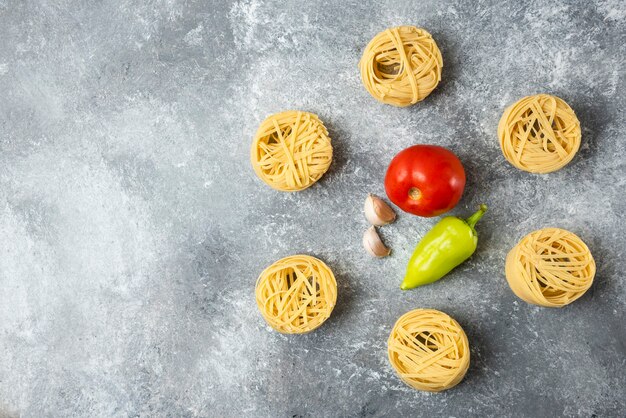 Tagliatelle nidi di pasta cruda e verdure su fondo di marmo.