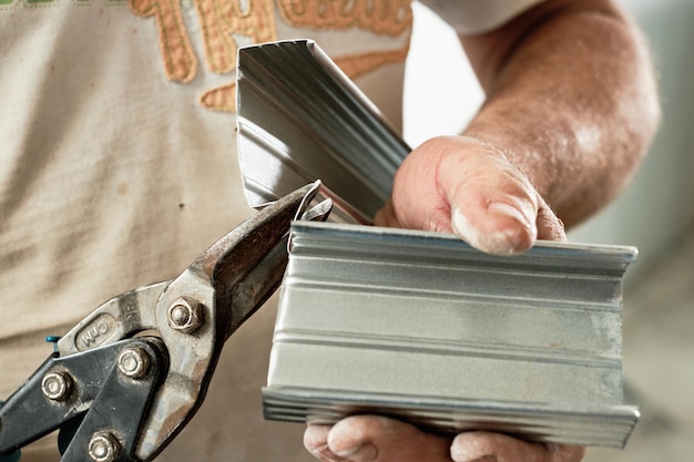 Taglio di profili in acciaio da un maestro, primo piano, messa a fuoco selettiva. Preparazione per l'installazione del telaio del sistema di profili del soffitto del muro a secco. Industria del rinnovamento e del rinnovamento