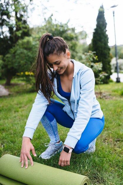 Tappetino da yoga o fitness pieghevole da donna dopo l'allenamento nel parco. Concetto di vita sana