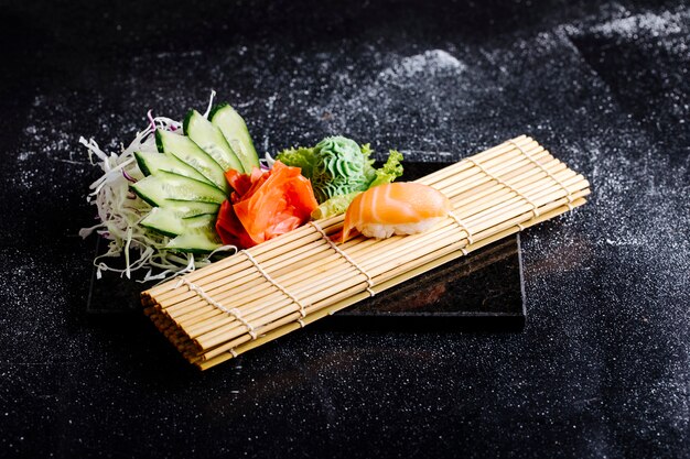 Tappetino per sushi, rotolo di salmone, wasabi, zenzero rosso marinato e fette di cetriolo.