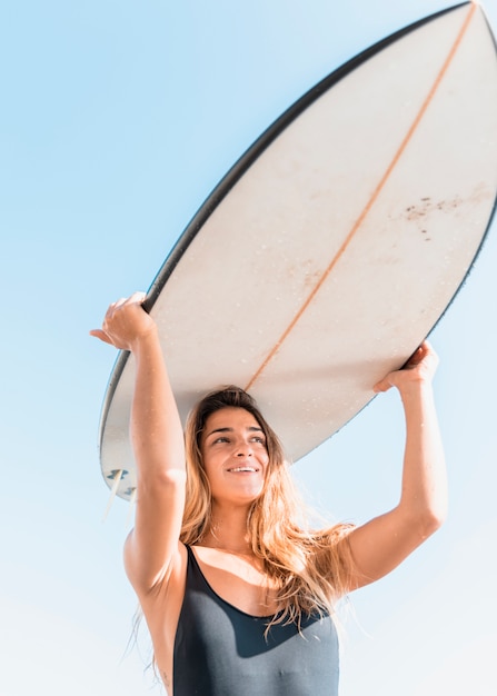 Tavola da surf della tenuta della giovane donna sulla testa