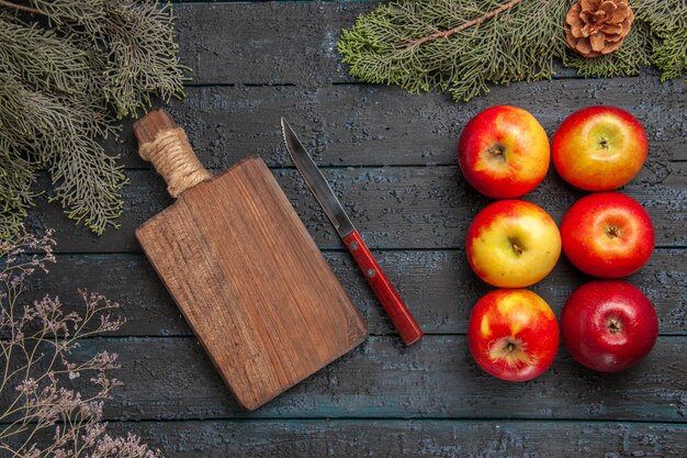 Tavola vista dall'alto e mele sei mele accanto al coltello e tagliere di legno sotto i rami con coni