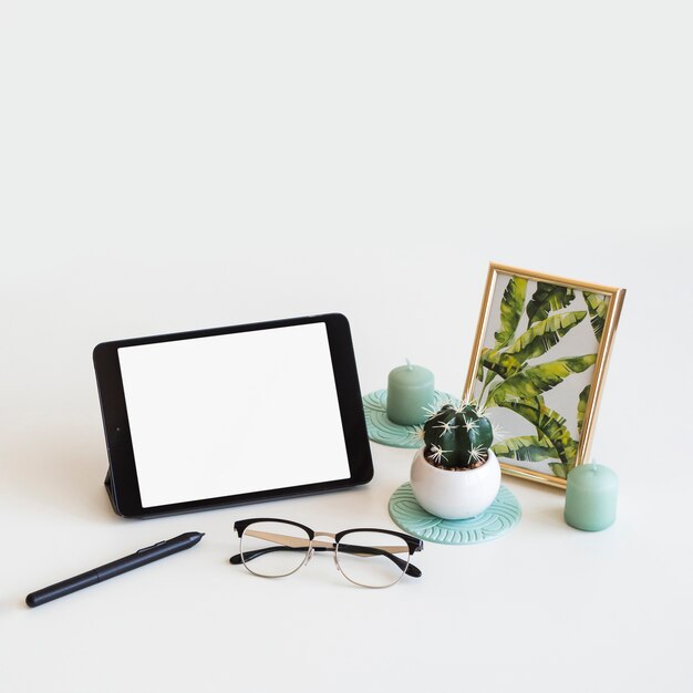 Tavolo con tablet vicino a cornice, penna e occhiali da vista