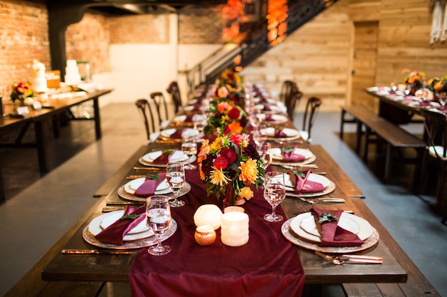 Tavolo lungo con piatti di lusso e decorato con fiori colorati e candele
