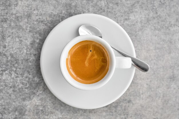 Tazza bianca con caffè espresso forte e profumato con schiuma densa in una tradizionale caffetteria greca Vista dall'alto del caffè con piattino sull'idea del tavolo in marmo grigio per sfondo o poster