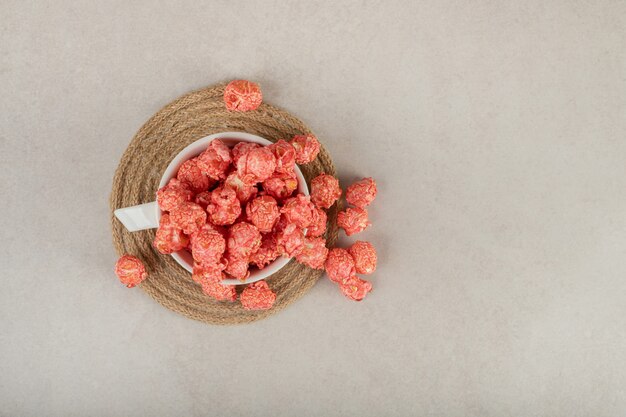 Tazza da tè su un sottopentola che scorre con popcorn rosso su marmo.