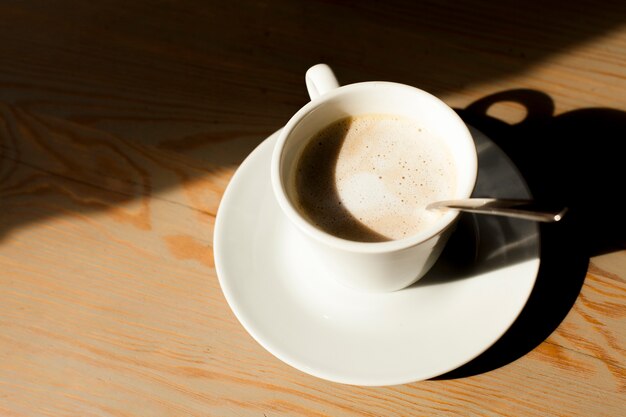 Tazza del caffè del latte con schiuma schiumosa su fondo di legno