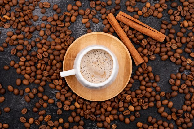 Tazza deliziosa del caffè del cappuccino circondata dai chicchi di caffè arrostiti sulla pietra nera