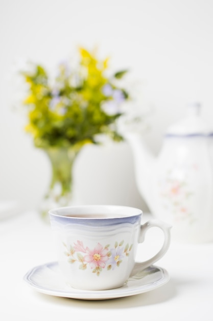 Tazza della porcellana di tè e piattino sulla tavola bianca contro fondo selettivo
