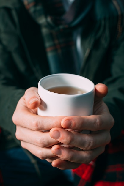 Tazza della tenuta della persona del primo piano con la bevanda calda