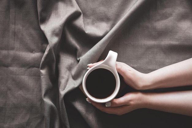 Tazza di caffè a letto in mani femminili distese