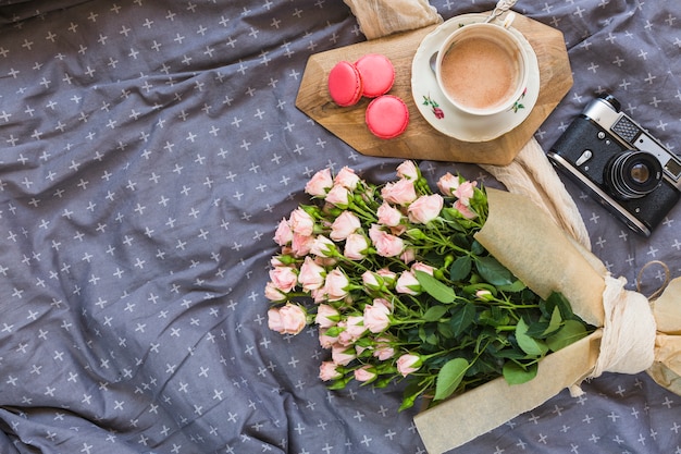 Tazza di caffè; amaretti; macchina fotografica e bouquet di fiori sulla tovaglia