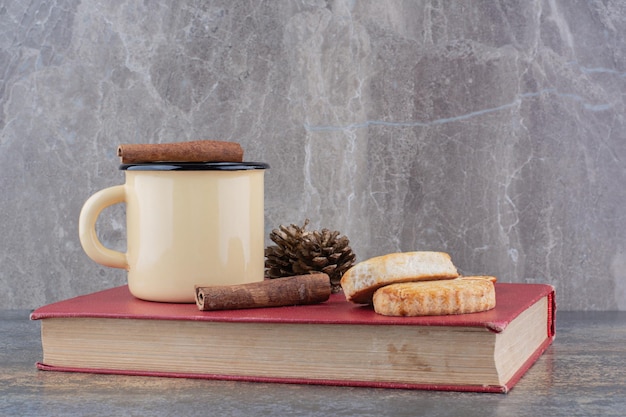 Tazza di caffè calda con bastoncino di cannella e biscotti sul libro. Foto di alta qualità