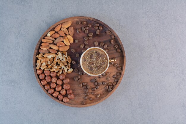 Tazza di caffè caldo schiumoso e vari dadi sul piatto di legno.