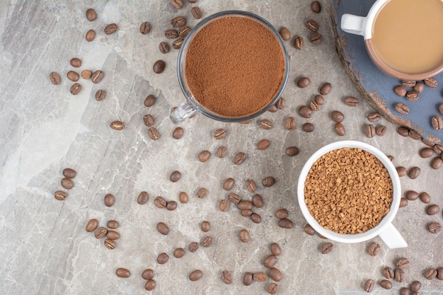 Tazza di caffè, chicchi di caffè e caffè macinato sulla superficie in marmo.